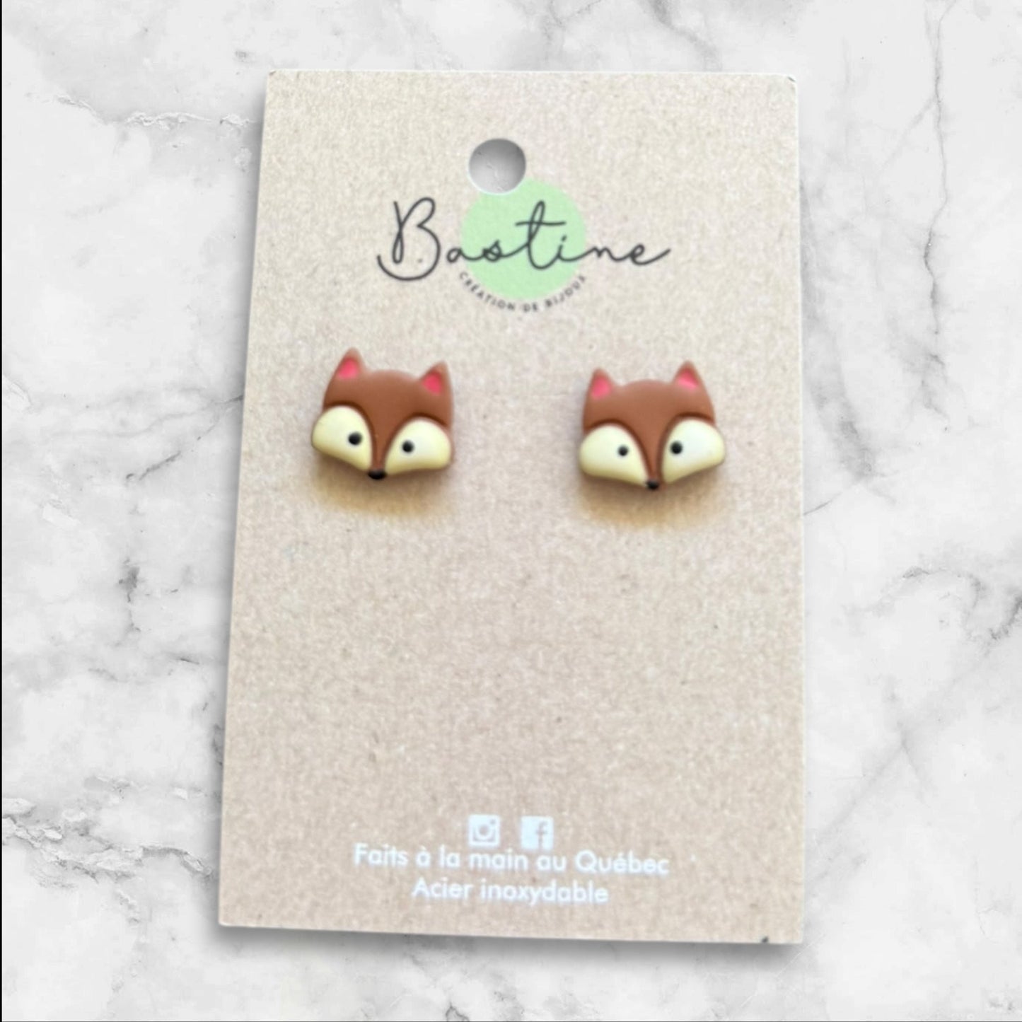 Pair of owl-shaped earrings on a branded card with a marble background