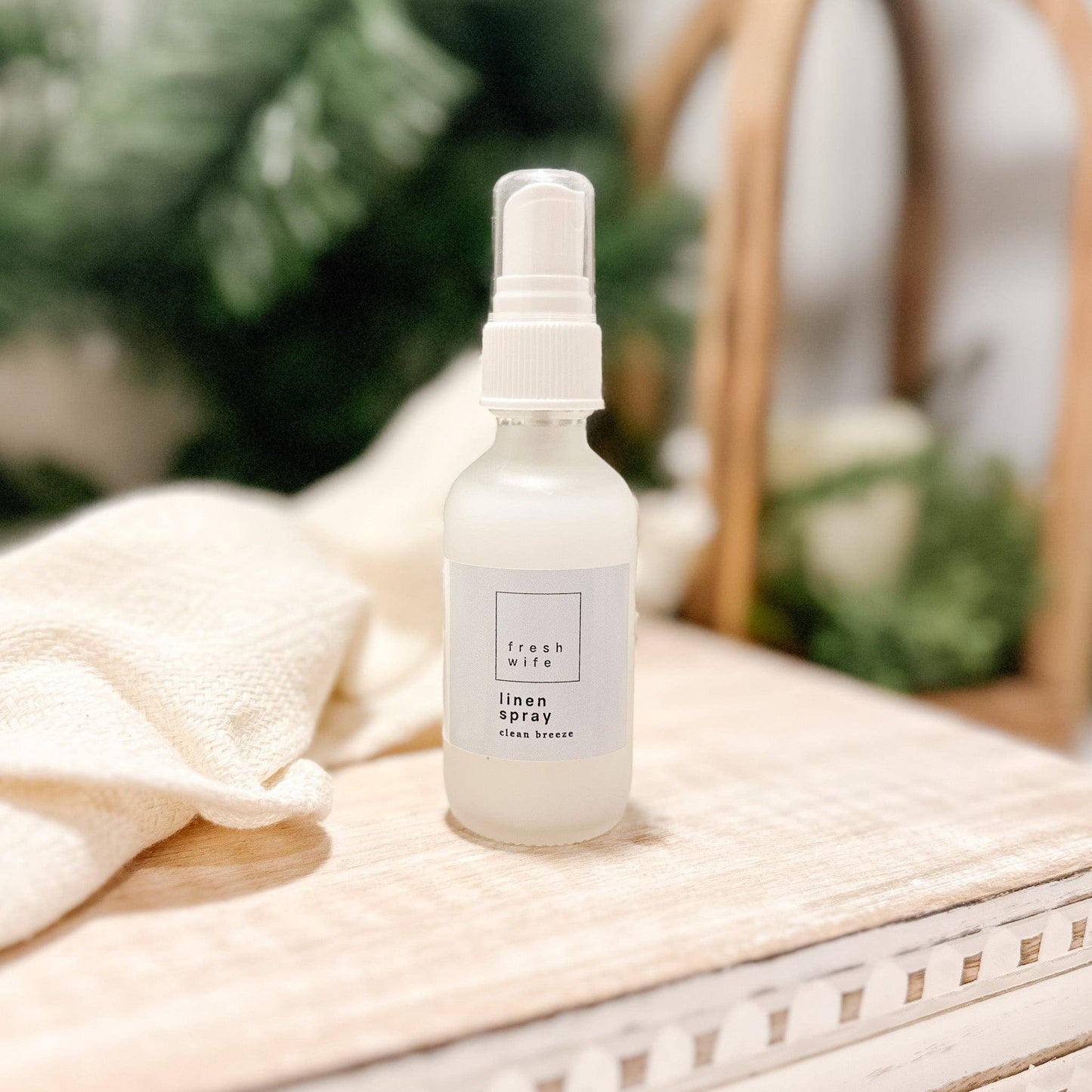 White spray bottle labeled 'Linen Spray' on a beige surface with greenery in the background