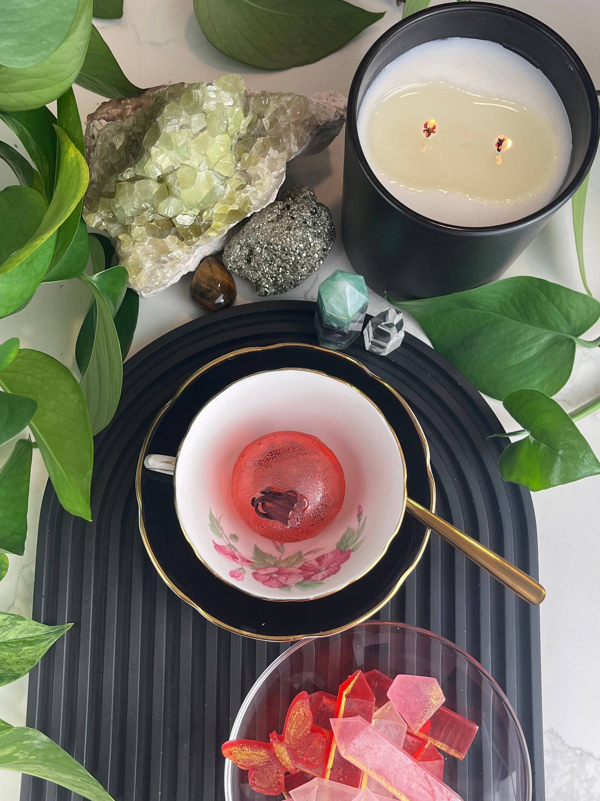 Candle, teacup with pink interior, and decorative items on a dark surface with green leaves.