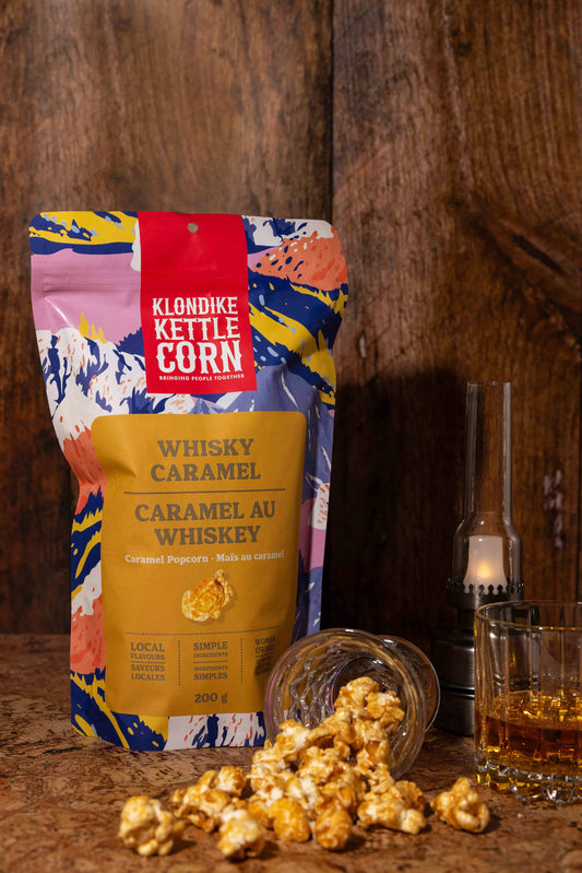 Klondike Kettle Corn Whisky Caramel package with popcorn and a glass of whiskey on a wooden surface.