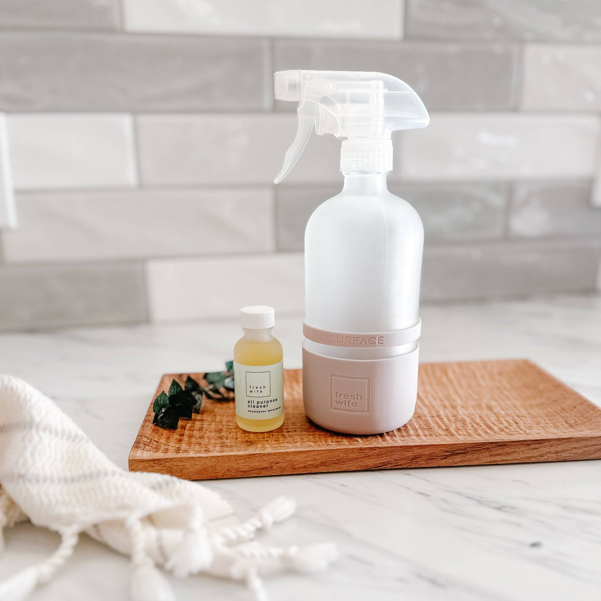 White spray bottle and small jar on a wooden tray with a tiled wall background